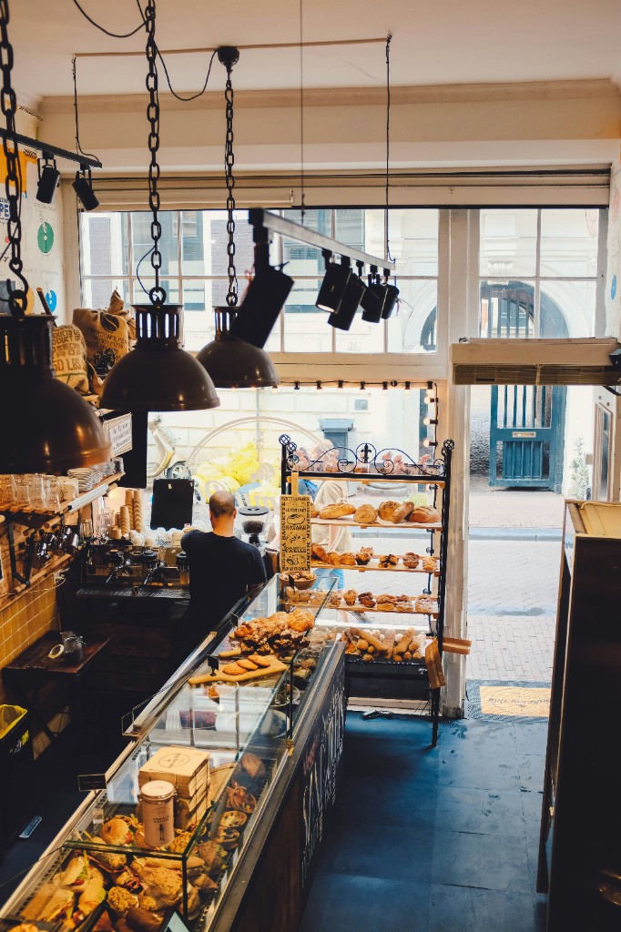 Bakery interior with glass pastry case, bread on racks, and warm pendant lighting.